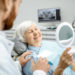 Elderly lady smiling while looking at dentures in a mirror at beach grove dental tsawwassen