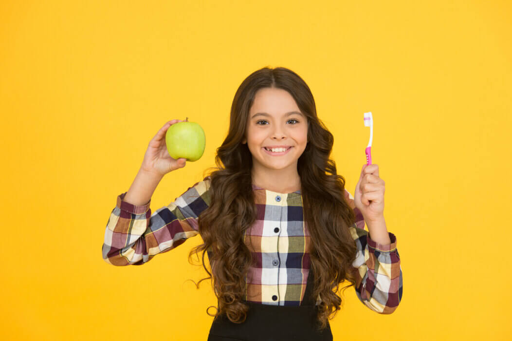 Beautiful natural smile. Happy child hold green apple and toothbrush. Little girl smile with brush and natural fruit. Natural dental care. Gentle natural way to white teeth.